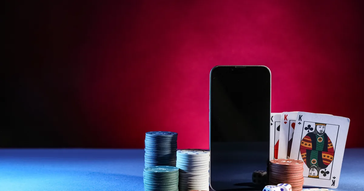 Smartphone auf einem Tisch, daneben ein Stapel Pokerchips und ein Kartenspiel
